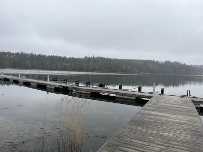 Stilla vårdag vid bryggan på Örnvikens Glamping med spegelblank sjö och dimmig skog
