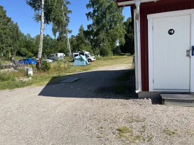 En enkel ställplats med toalettbyggnad, några husbilsgrannars tält och bilar i sommarsolen